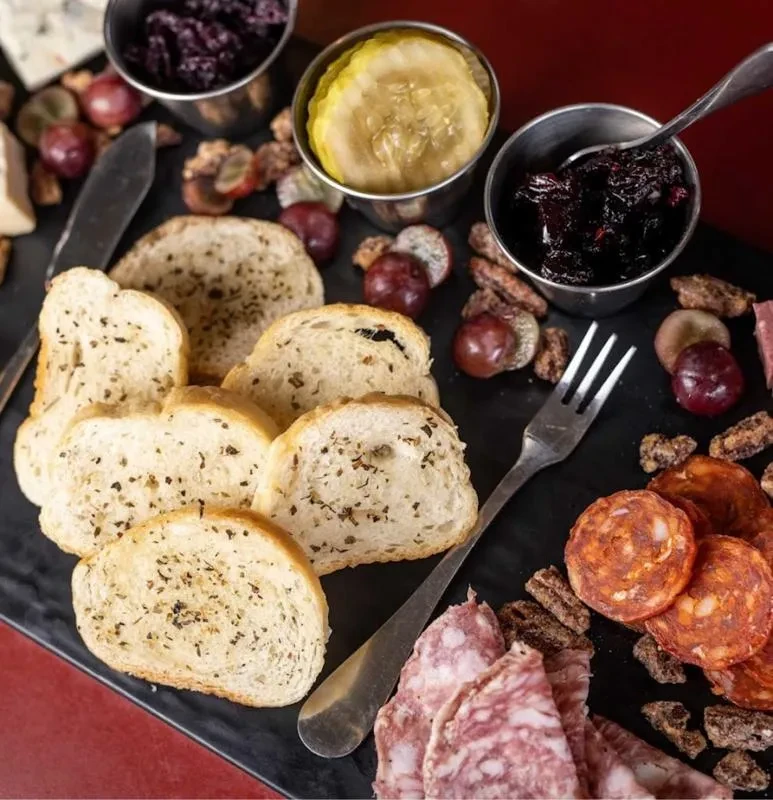 Meticulously arranged charcuterie board with meats, cheese, bread, grapes, and condiments.