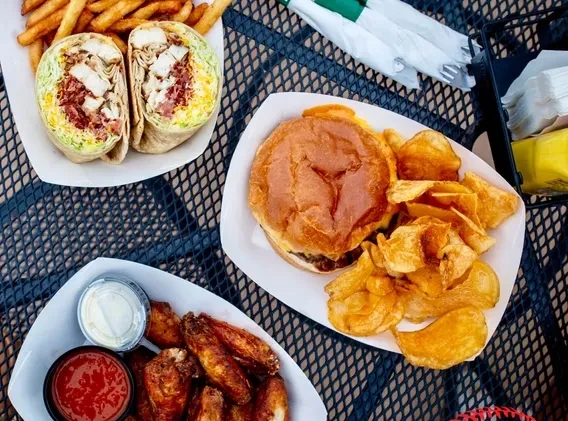 Top-down: Chicken wrap, fries, wings, burger, and chips on a table.