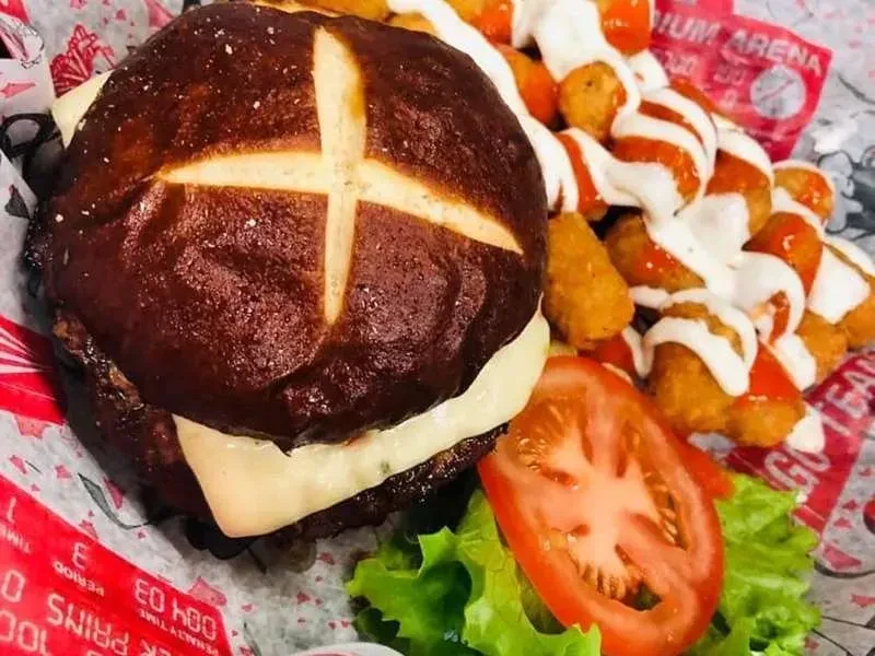 Pretzel bun burger, melted cheese, and sauced tots on a sports liner.