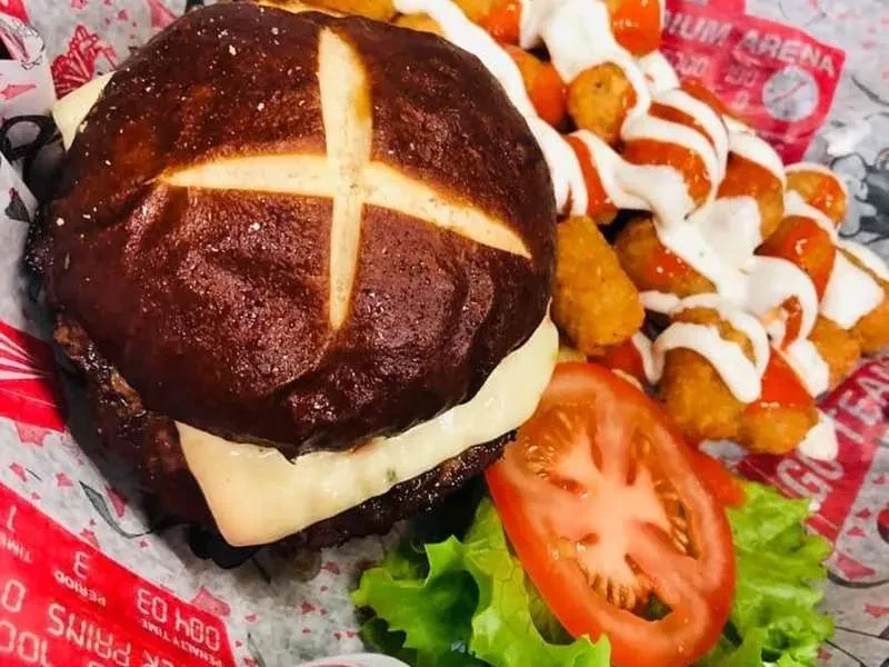 Overhead view: Pretzel bun burger, sauced potato bites, lettuce, and tomato.