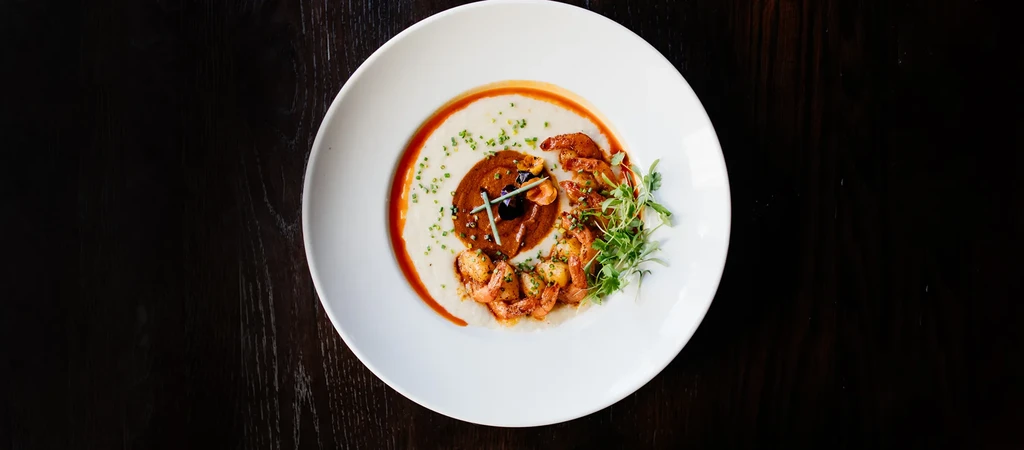 Creamy grits, shrimp, rich sauce with dark garnish, and green herbs.