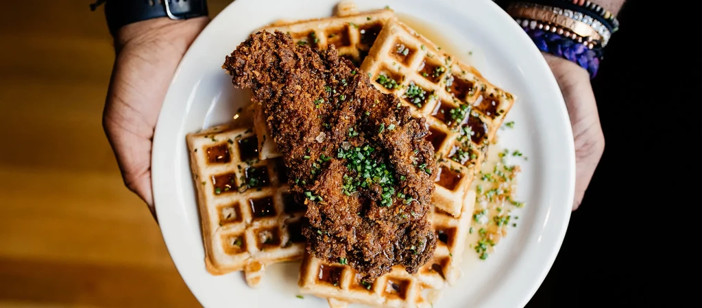 Crispy fried chicken and waffles with syrup and chives.