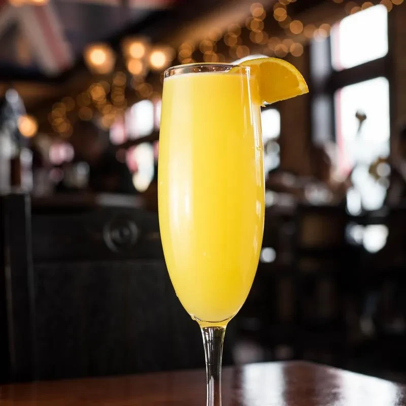 Mimosa cocktail with orange slice on wood, blurred bokeh, Union Jack hint.