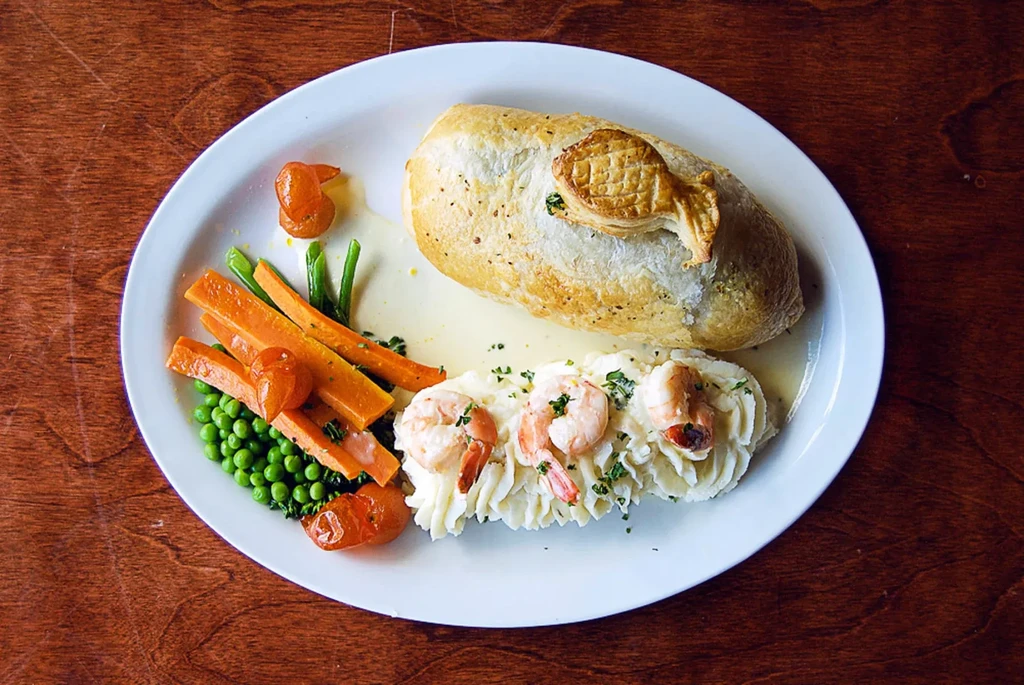 High-angle, close-up of gourmet Wellington, shrimp, mashed potatoes, and vegetables.