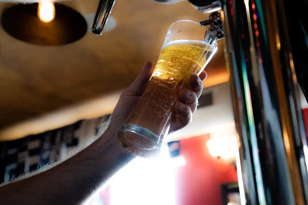 Hand holds glass as golden beer pours from a tap.