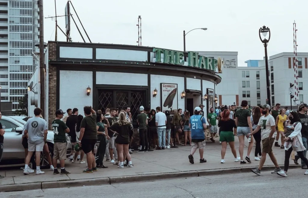 Lively crowd in green outside The Harp pub building.