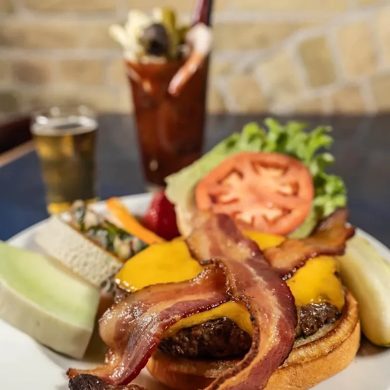 Double cheeseburger with bacon, salad, cantaloupe, pickle, and two drinks.