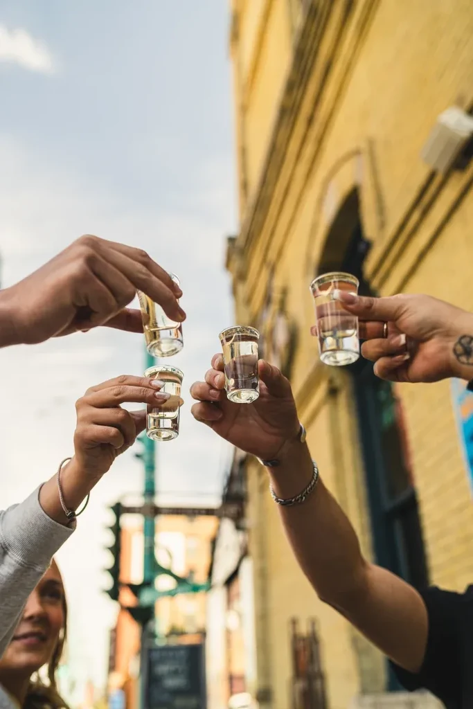 Four hands holding shot glasses in an urban outdoor toast.