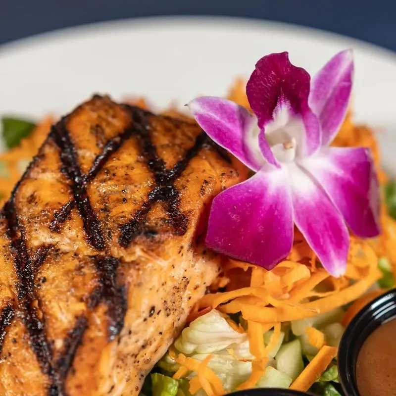 Close-up of grilled salmon, fresh salad, an orchid, and sauce.