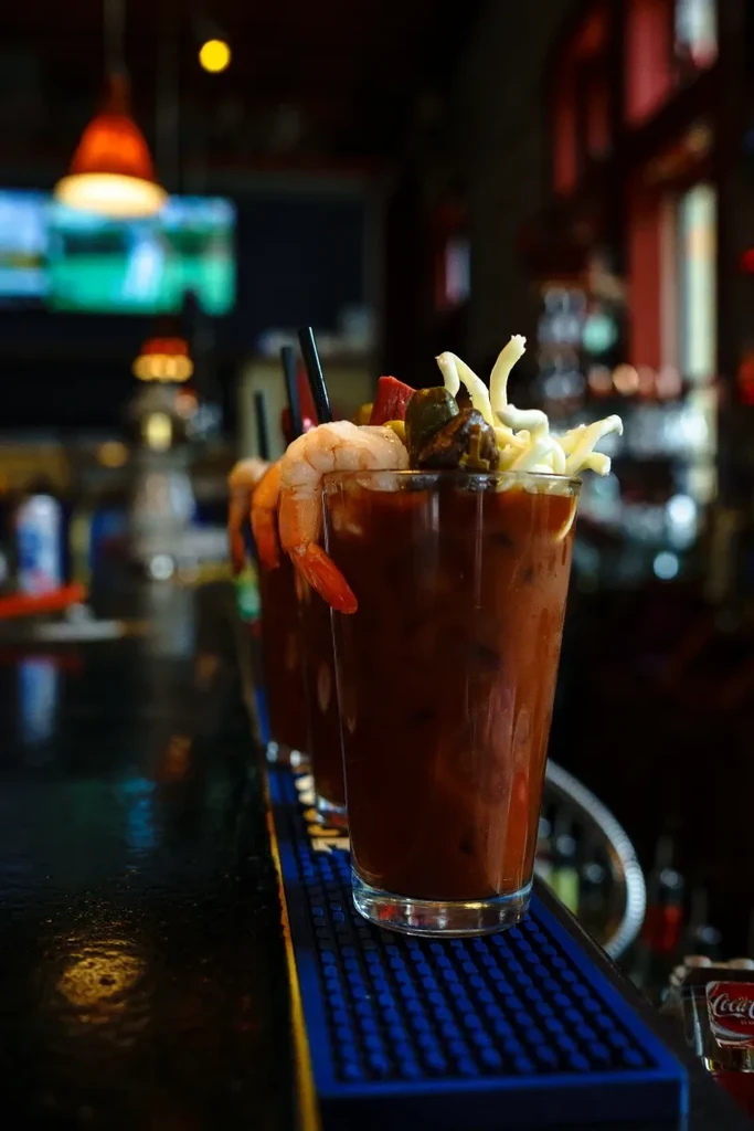 Row of elaborately garnished Bloody Mary cocktails on a dark bar counter.