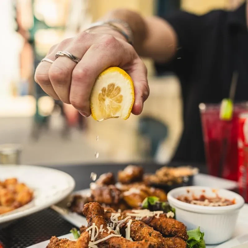 Jeweled hand squeezes lemon juice over fried food, cheese, and lettuce.
