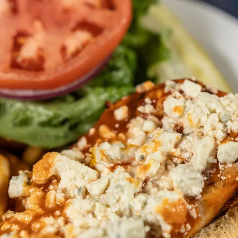 Buffalo chicken sandwich topped with blue cheese crumbles, with a side of fries.