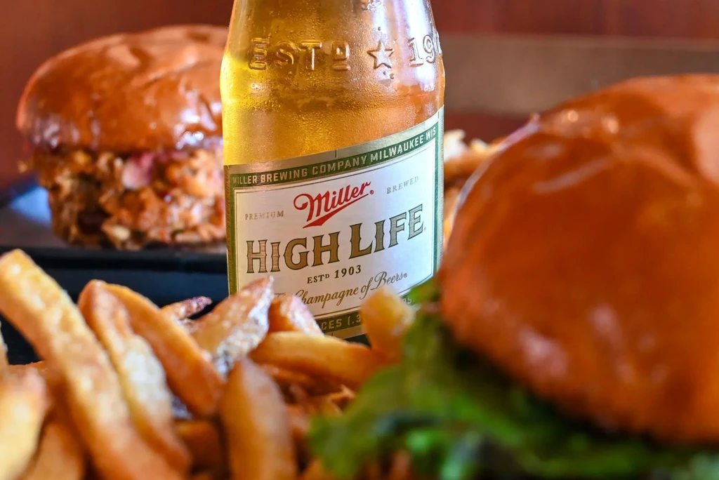Cold Miller High Life bottle, golden fries, and burgers on a table.