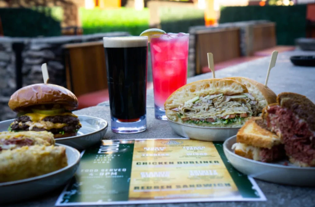 Outdoor table with cheeseburger, sandwiches, beer, cocktail, and menu.