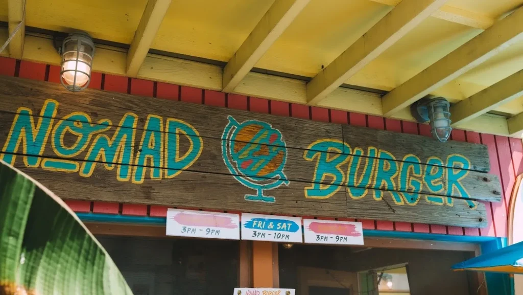 Rustic "Nomad Burger" sign on a red and yellow restaurant exterior.