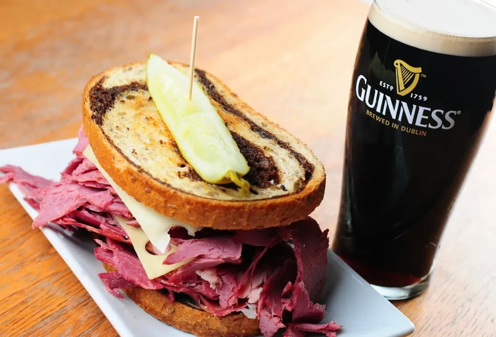 Marbled rye Reuben sandwich with pickle and a pint of Guinness.