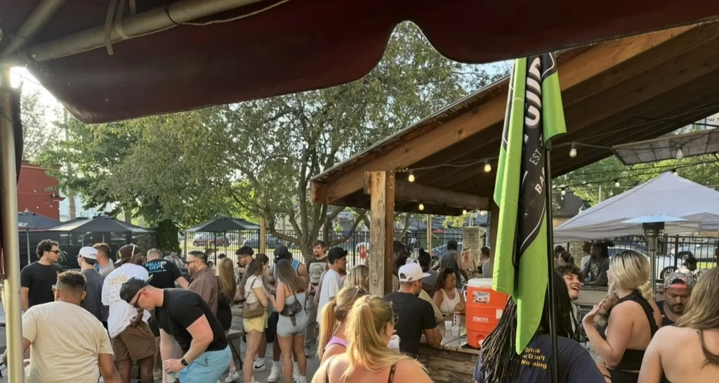 Lively outdoor gathering with people around a bar under string lights.