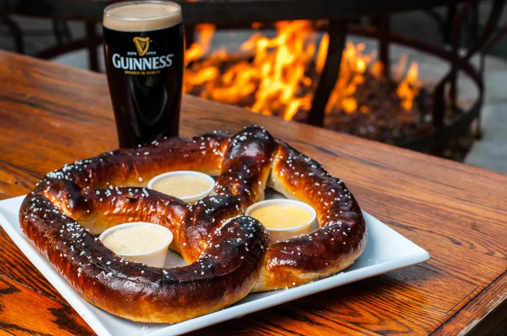 Freshly baked pretzel, sauces, and Guinness beer by a warm fire pit.