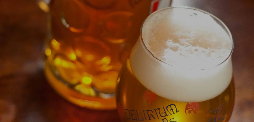 Delirium beer in a tulip glass, blurred stein, warm pub lighting.