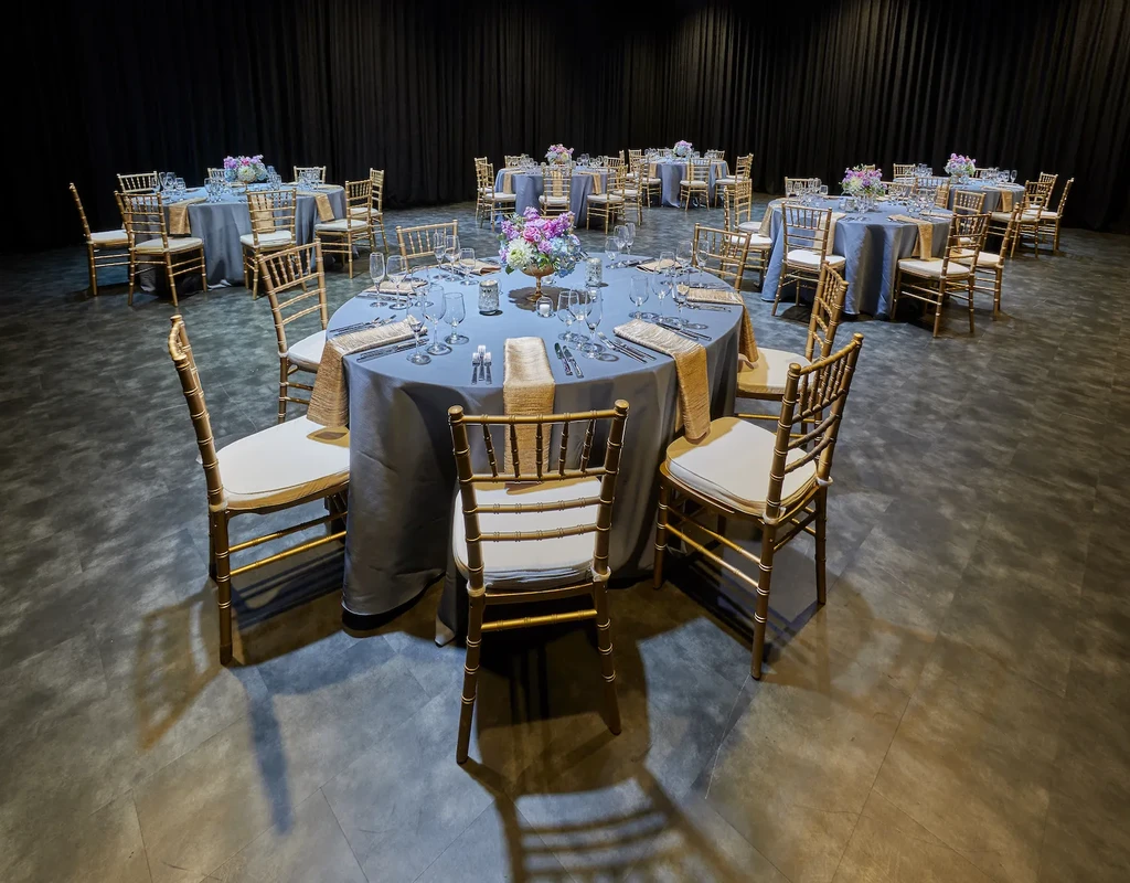 Meticulously set event hall with gold Chiavari chairs and floral centerpieces.