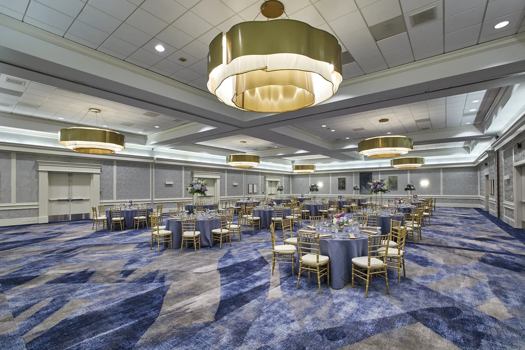 Empty elegant ballroom with blue tables, gold chairs, and ornate chandeliers.