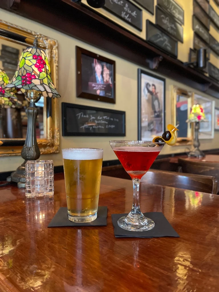Light beer and cherry-garnished red cocktail on a cozy bar.