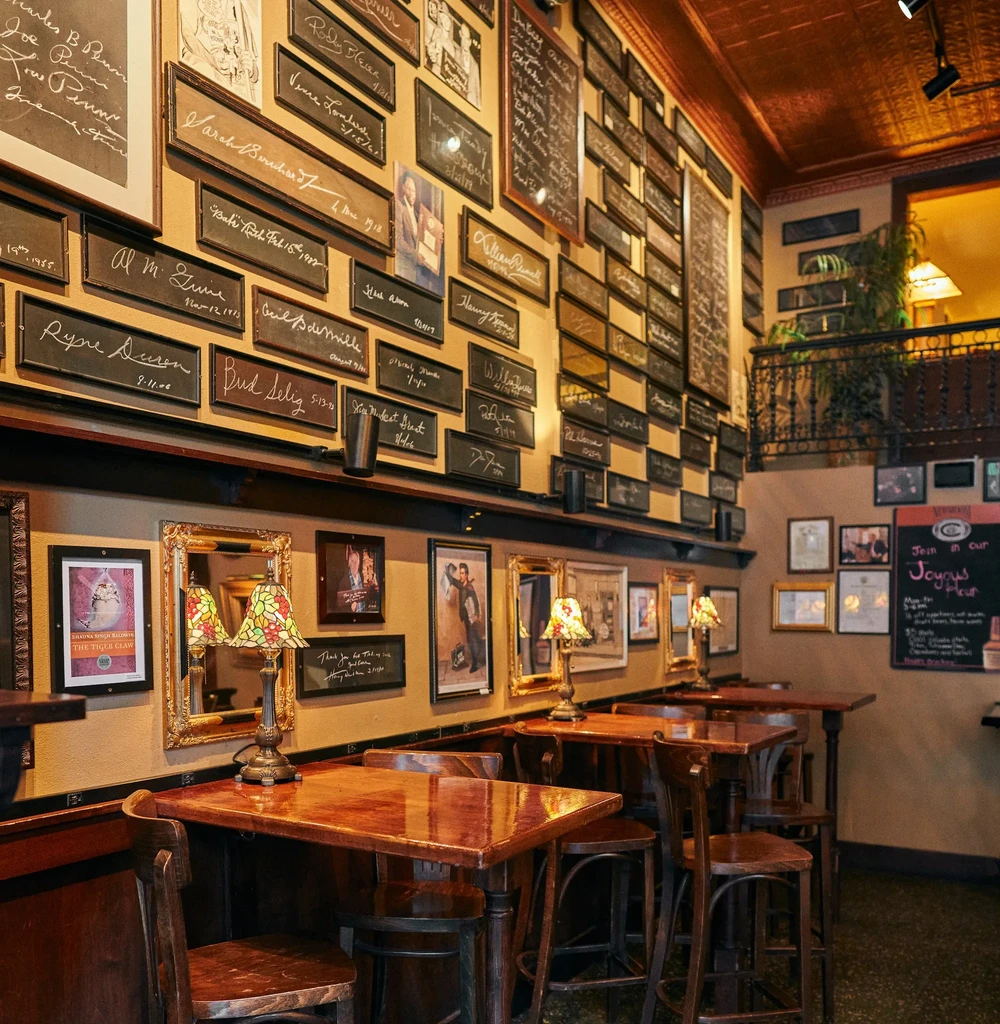 Warm restaurant interior with signed plaques, Tiffany lamps, and wood tables.