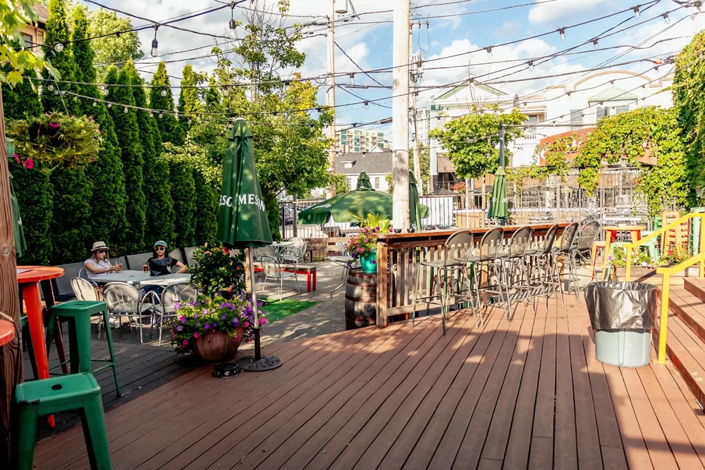 Sunny outdoor restaurant deck with bar, seating, people, and green umbrellas.