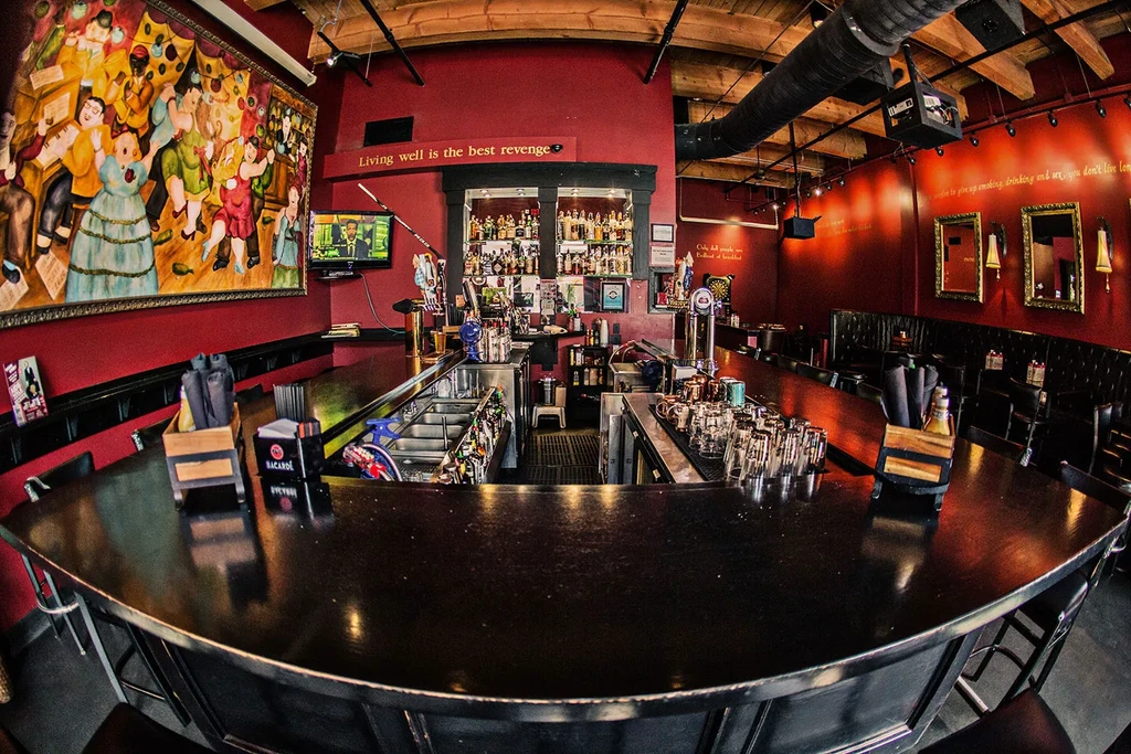 Fisheye view of a well-stocked bar, dark counter, red walls, folk art.