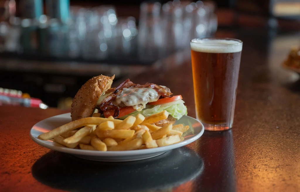 Gourmet burger, fries, and a cold amber beer on a white plate.