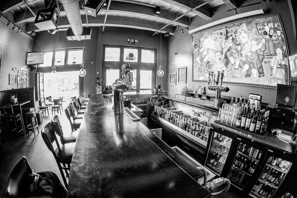 Black and white restaurant bar with long counter and a vibrant mural.
