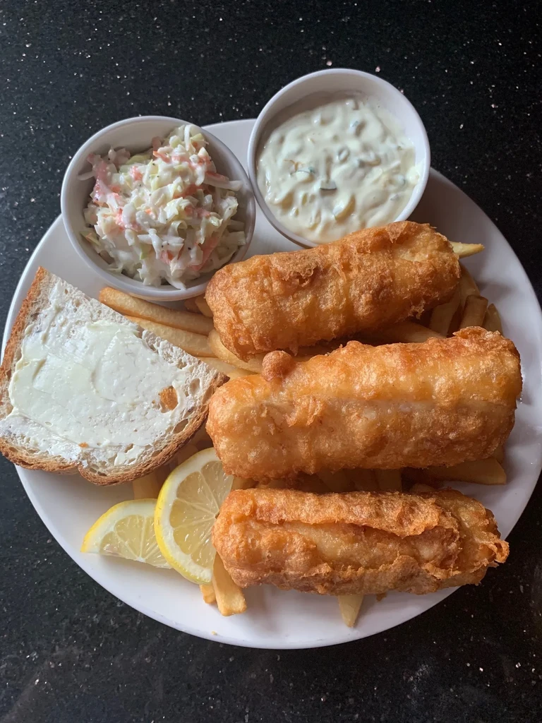 Fish and chips, coleslaw, tartar sauce, brown bread, and lemon wedges.
