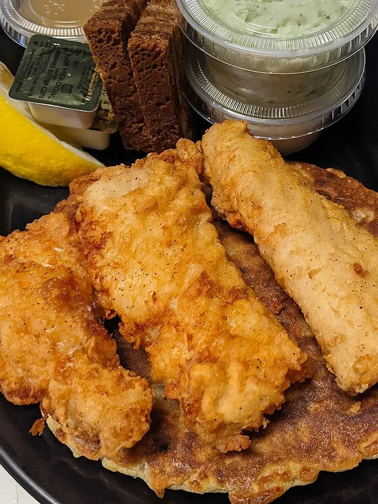 Fried fish on a savory pancake with lemon, sauces, and rye bread.