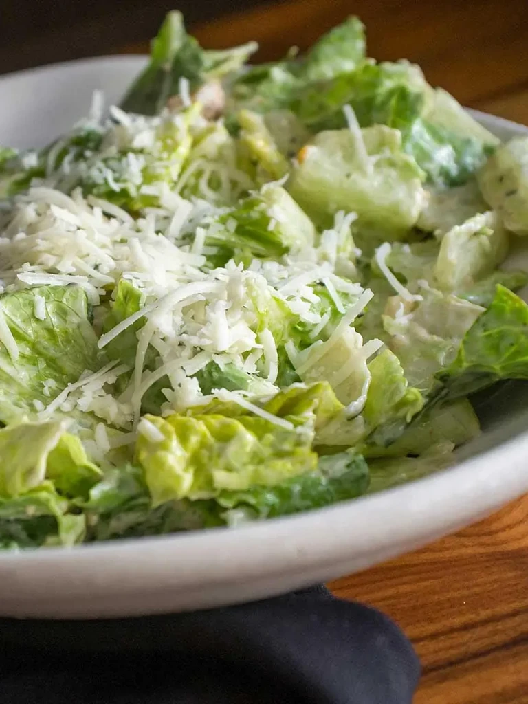 Green salad in a white bowl with creamy dressing and shredded cheese.