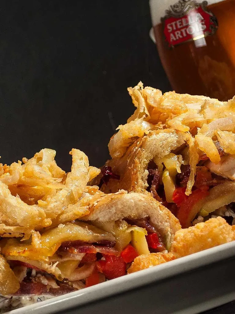 Overflowing sandwich with crispy fried onions and Stella Artois beer.
