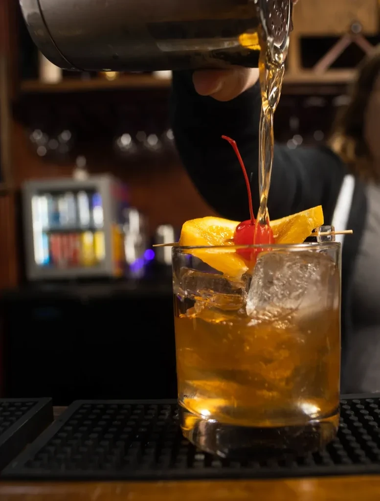 Bartender pours golden cocktail into glass with ice and garnish.
