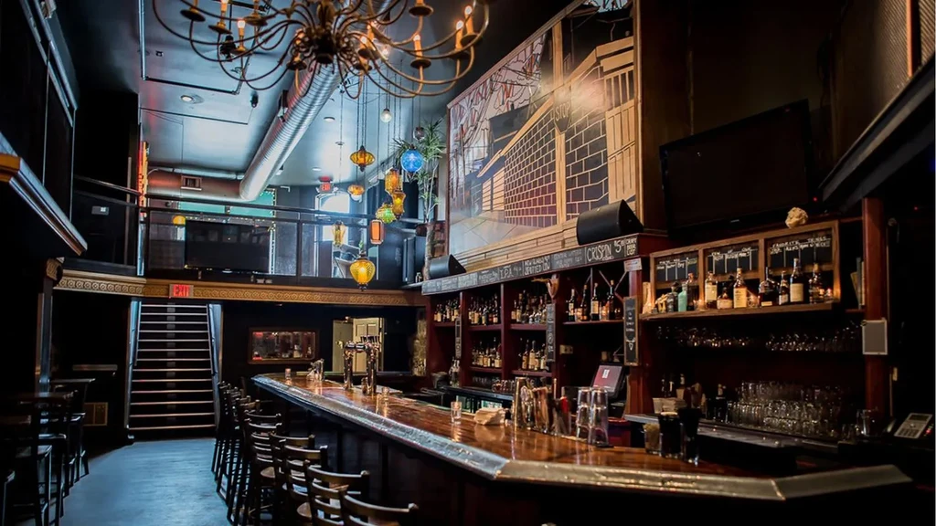Empty, dimly lit bar with wooden counter, ornate lighting, and urban mural.
