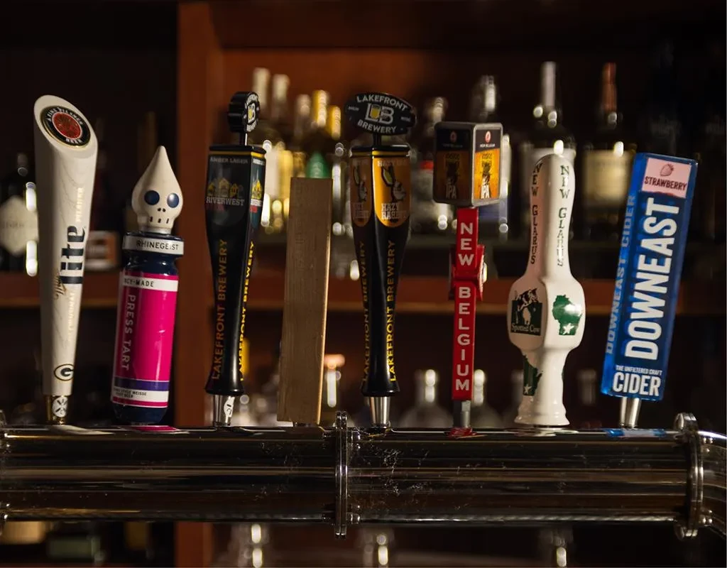 Seven diverse beer and cider tap handles on a bar.