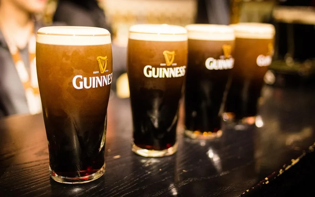 Four Guinness stouts with creamy heads on a dark bar.