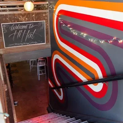 Vibrant stairwell entrance to Hi-Hat restaurant, with mural and chalkboard sign.