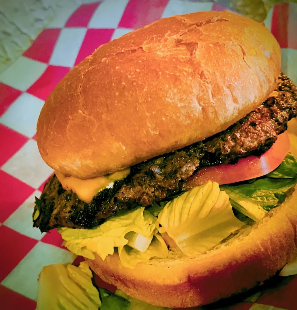 Burger with bun, patty, cheese, tomato, lettuce on checkered surface.