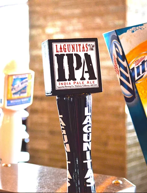 Lagunitas IPA beer tap handle in focus at a bar counter.