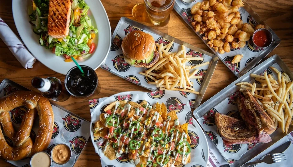 Overhead: Wooden table laden with diverse casual food and drinks.
