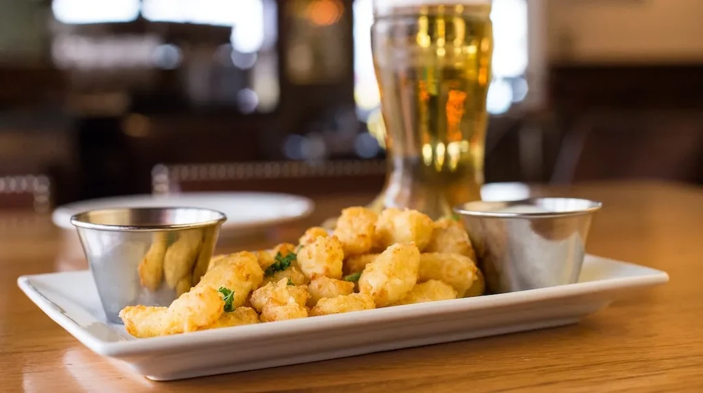 Golden fried food, sauces, and an amber beer on a wooden table.