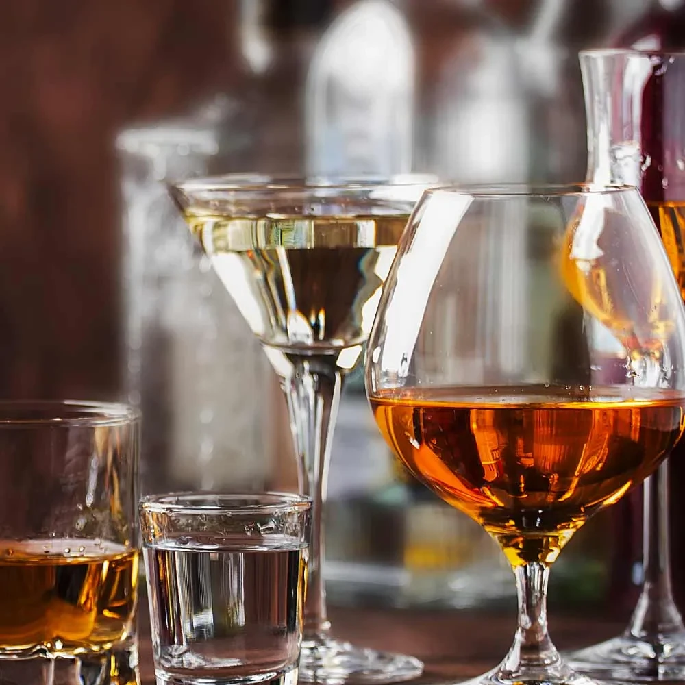 Several glasses with different clear and amber spirits on a bar.