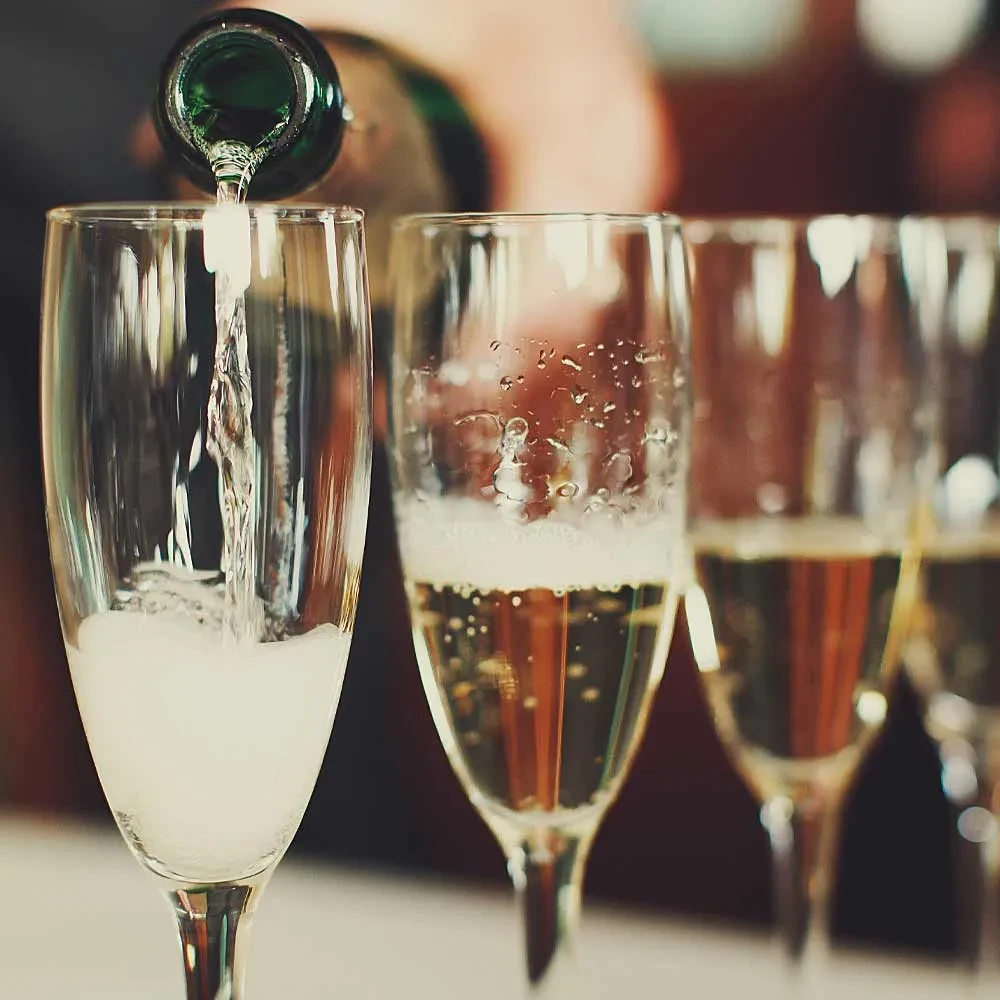 Sparkling champagne pours into a flute, with two other sparkling flutes.