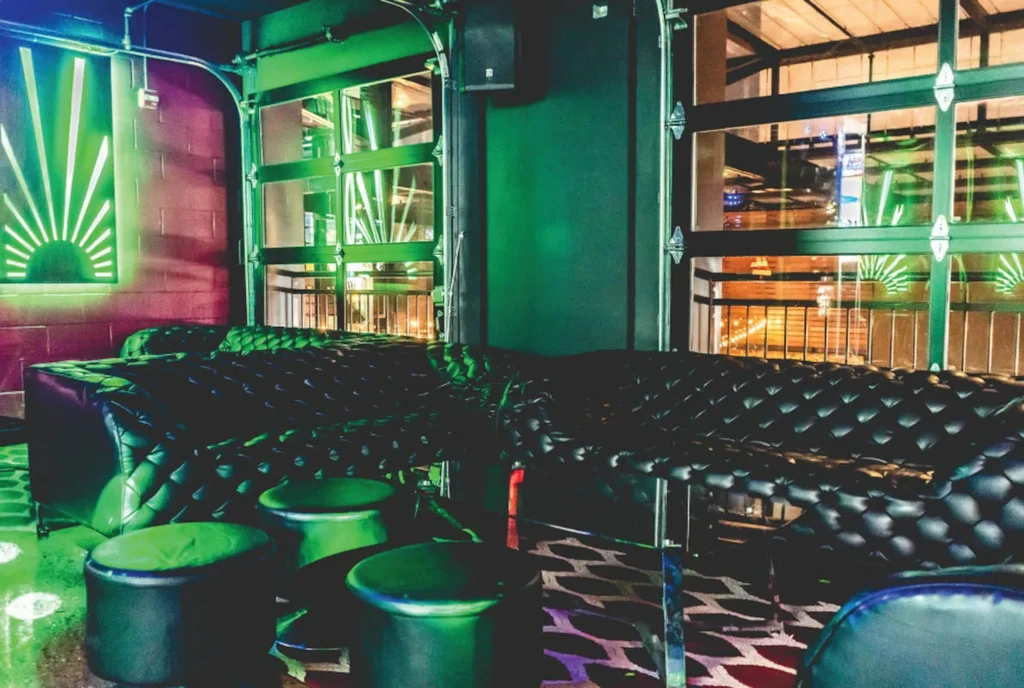 Dark, industrial lounge with black tufted seating and vibrant green lighting.
