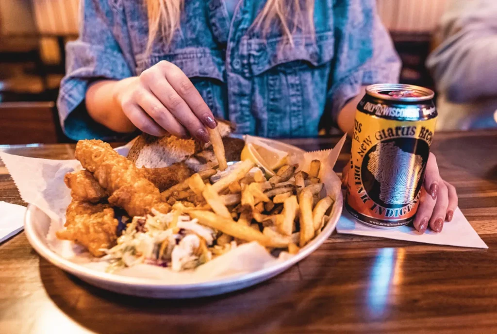 Hands picking fry from fish and chips, New Glarus beer.