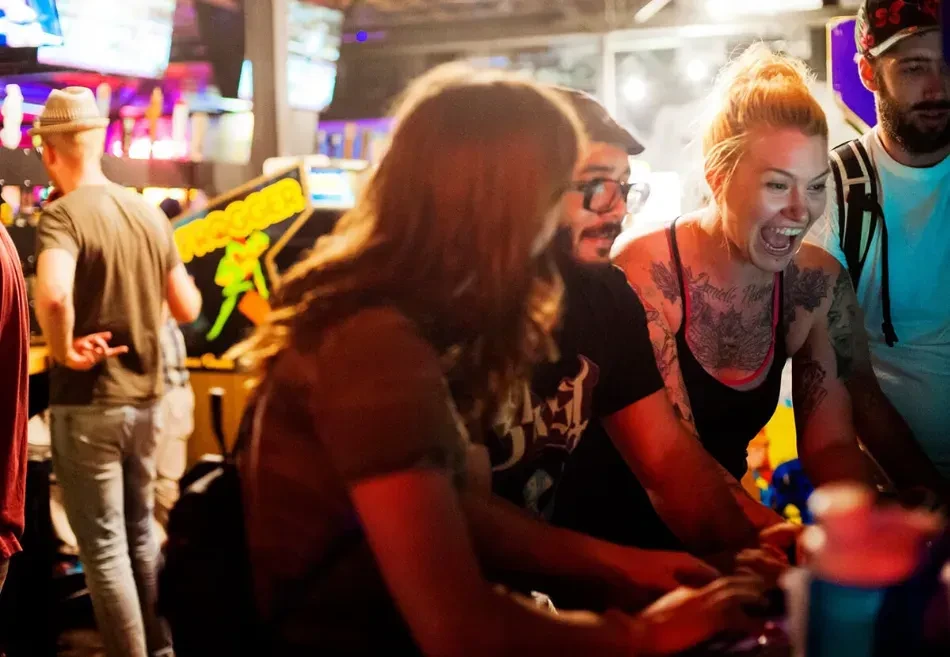 Laughing blonde woman plays Frogger arcade game in an arcade bar.