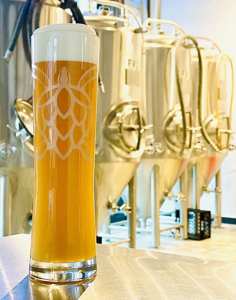 Golden beer glass with turtle-hop logo, FV2 fermentation tanks in brewery.